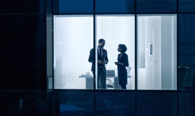 Two people standing in a room with one of them talking to another person.