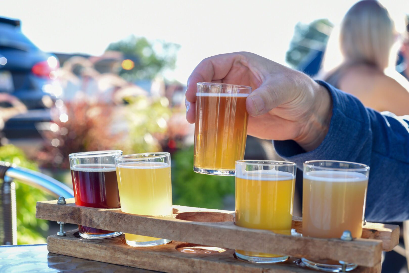 A person holding up a beer in front of several glasses.